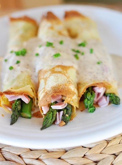 White plate with three savory crepes stuffed with ham and asparagus lined up next to each other.