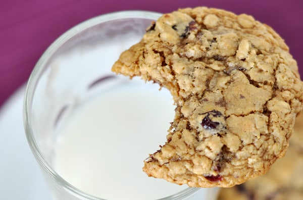 An oatmeal cookie with a bite taken out over a glass cup of milk.