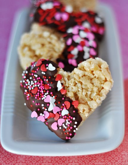 White tray with heart-shaped rice krispie treats half dipped in chocolate and sprinkles.