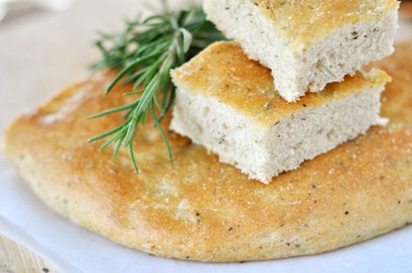 A flat disk of herbed focaccia bread with two squares of the bread on top.