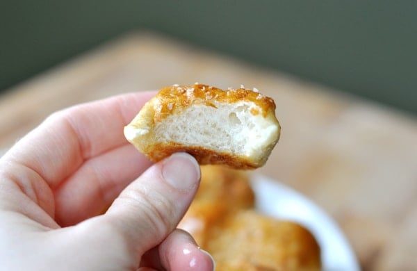 A hand holding a pretzel bite with a bite taken out. 