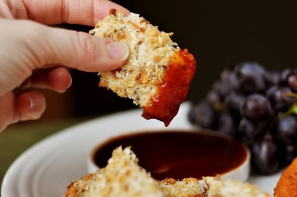 A homemade crispy chicken nugget being dipped in barbecue sauce.