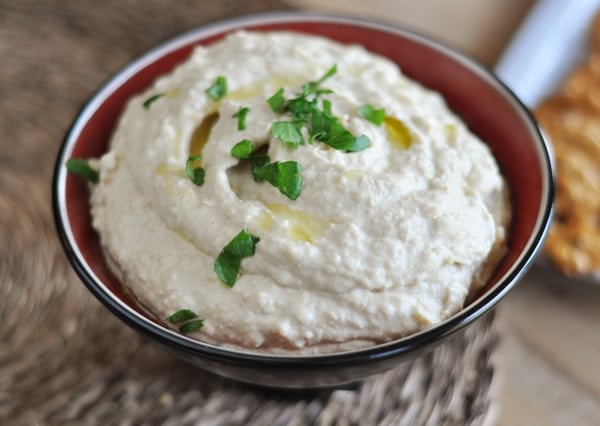 Bowl of hummus topped with drizzled oil and cilantro pieces.