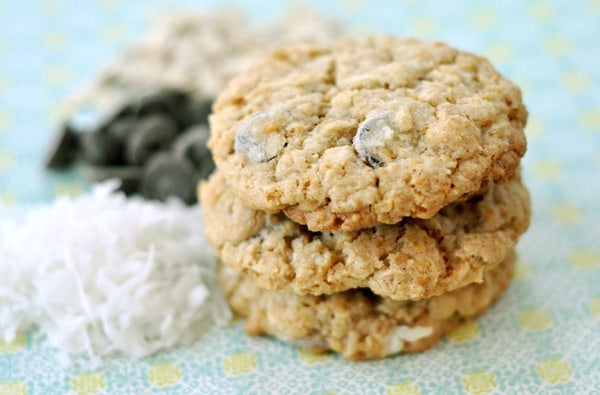 A stack of chocolate chip cookies next to piles of coconut and chocolate chips.