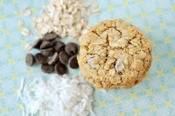 Top down view of a stack of cookies next to piles of shredded coconut, chocolate chips, and sliced almonds.