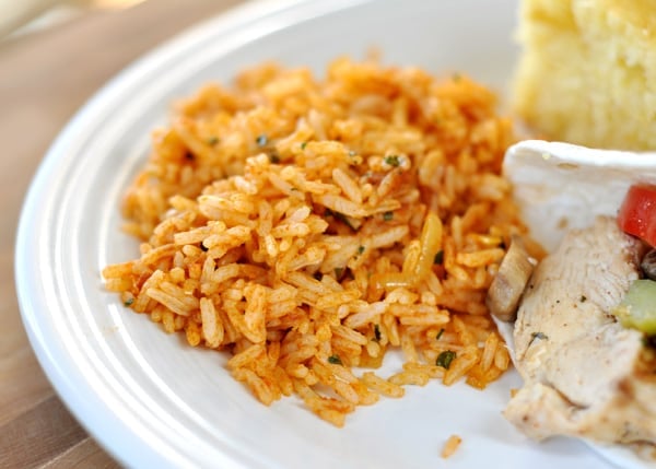 A white plate with a scoop of Mexican rice next to a chicken fajita and slice of cornbread.