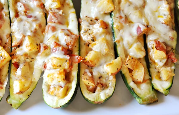 Stuffed baked zucchini lined up on a white platter.