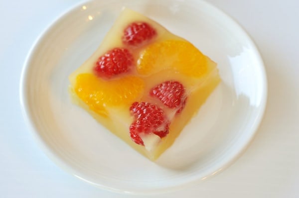 Top view of a piece of jello with raspberries and mandarin oranges in it.