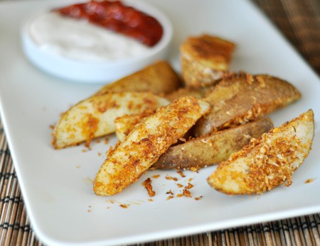 White rectangular platter with baked panko-crusted potato wedges and a small bowl of dipping sauce.