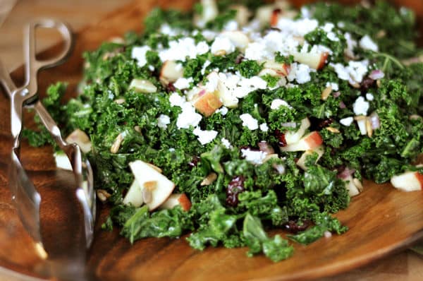 A kale and craisin salad with feta cheese and diced apples in a wooden salad bowl.