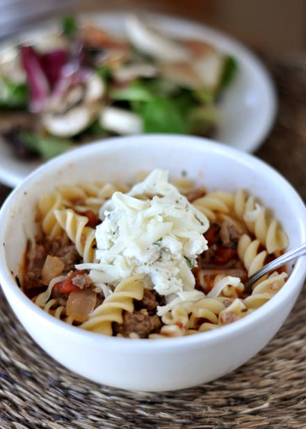 White bowl of lasagna soup and a green salad in the background.