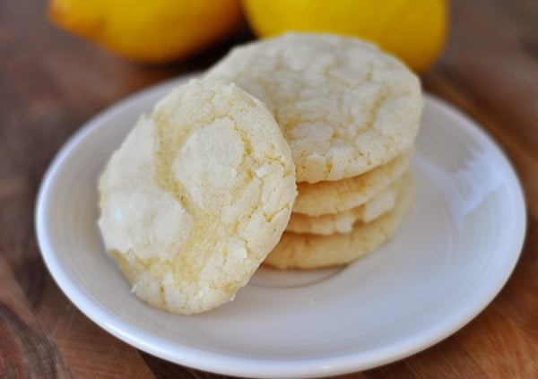 White plate with lemon crinkle cookies stacked on top of each other and one leaning on the stack.