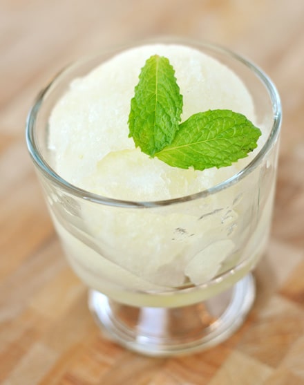 A small glass goblet filled with lemon ice and topped with mint leaves.