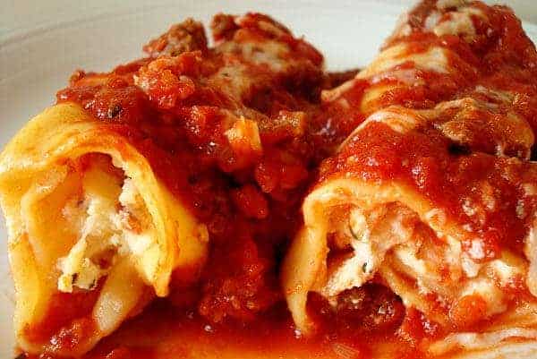 two manicotti pasta rolls with red sauce on top on a white plate