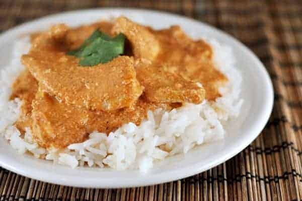 White rice with chicken and orange tikka sauce on top on a white plate.