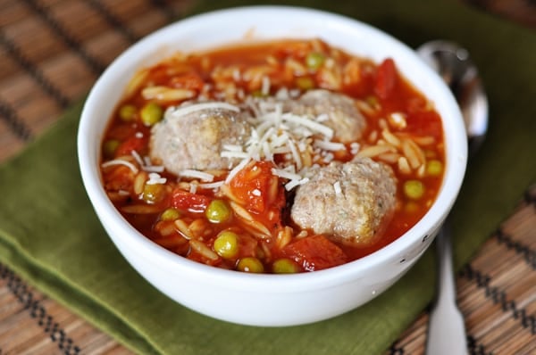 A white bowl full of pea and orzo soup with three meatballs nestled in the middle.