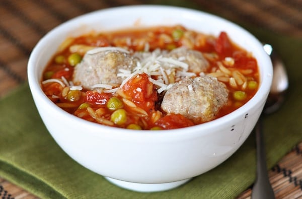 Side view of a white bowl full of orzo and meatball soup.