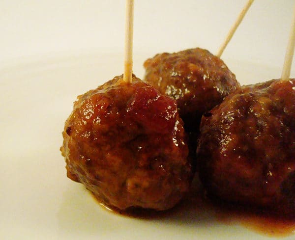 Meatballs covered in sauce with toothpicks in them on a white plate.