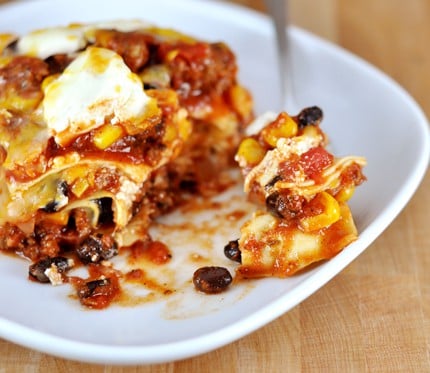 White plate with red sauce Mexican lasagna filled with beef, black beans, and corn.