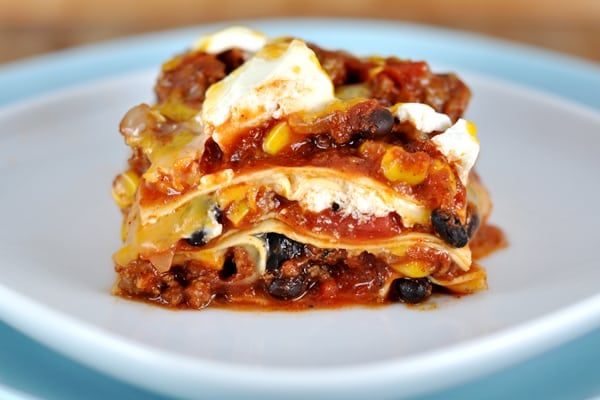 White plate with a piece of Mexican lasagna layered with noodles, corn, black beans, and cheese.