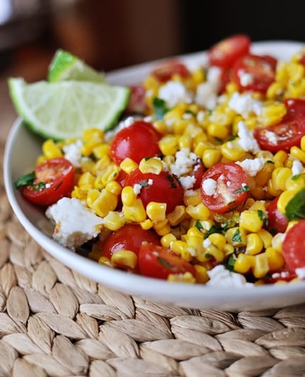 White bowl with corn and tomato Mexican salad with lime wedges on the side.