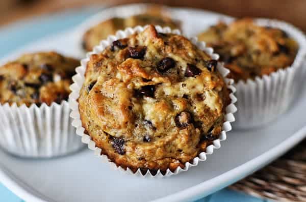 White plate with four chocolate chip banana bran muffins in white liners and one tipped to the side.