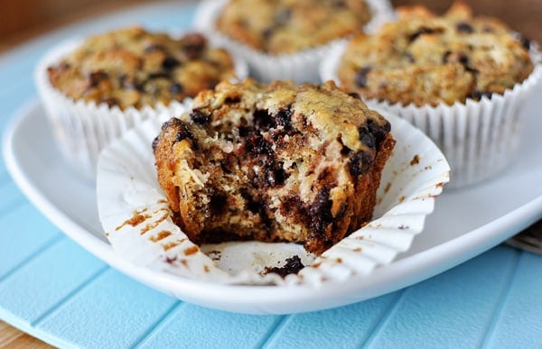 White plate with banana bran muffins in white liners, the muffin in front has a bite taken out and the liner is pulled off.