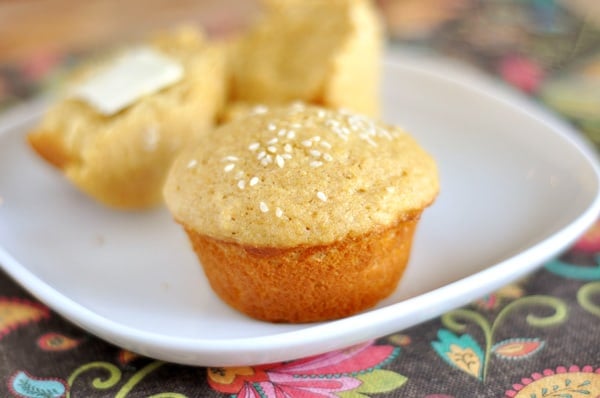 A sesame seed topped muffin in front of a muffin split in half on a white plate.