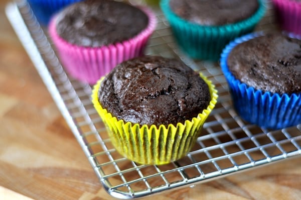 A cooling rack with chocolate muffins in colorful muffin liners on it.