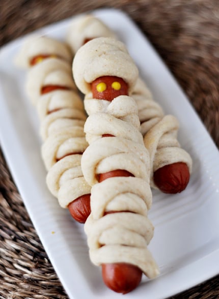 Hot dogs wrapped in breadstick dough to look like mummies on a white platter.