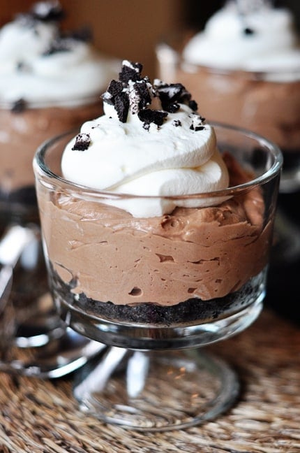 Clear white goblet with no-bake nutella cheesecake with an Oreo crust, and topped with whipped cream and crushed Oreo.
