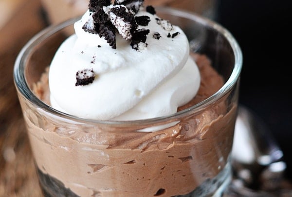 Individual chocolate no-bake cheesecake in a glass goblet topped with whipped cream and crushed Oreo.