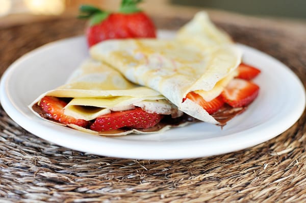 White plate with two strawberry and Nutella stuffed crepes.