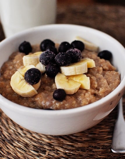 White bowl of cooked oatmeal topped with bananas and blueberries.