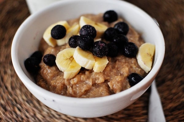 Top view of a white bowl full of cooked oatmeal topped with sliced bananas and blueberries.