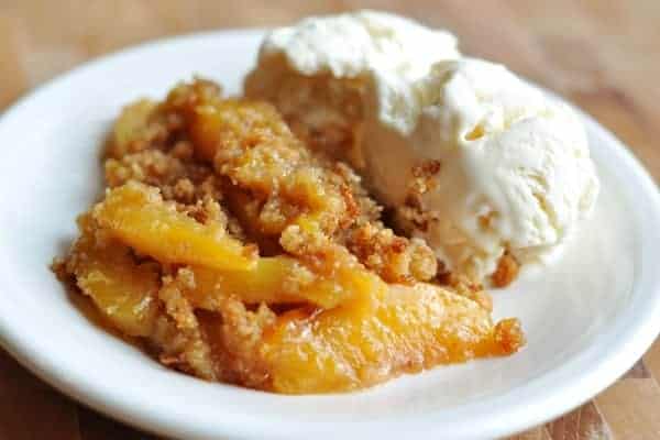 Peach cobbler and vanilla ice cream on a white plate.
