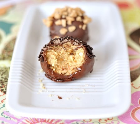 Chocolate-dipped bonbons in a row, one with a bite taken out, on a white rectangular dish.