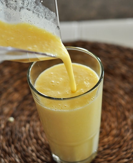 a tall glass cup that has orange julius mixture being poured into it