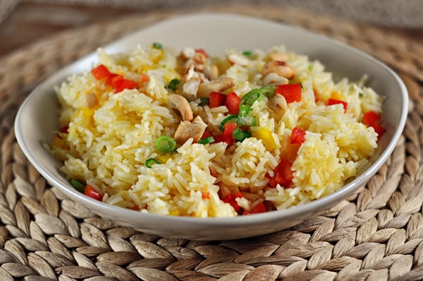 White bowl with cooked jasmice rice with orange flavoring and chopped peppers, cashews, and chives.