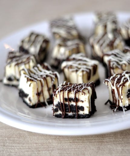 White plate with squares of oreo cheesecake bites drizzled with chocolate.