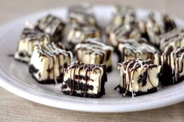 white plate with Oreo-studded cheesecake bites drizzled with white and dark chocolate