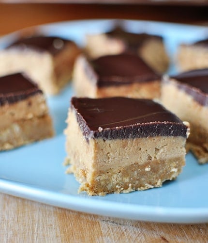 Blue plate with three-layer peanut butter chocolate bars cut in small squares.