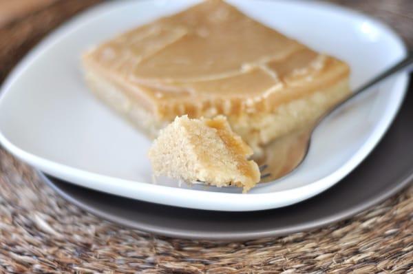 A piece of sheet cake with peanut butter frosting on a white plate, with a bite taken out on a fork.