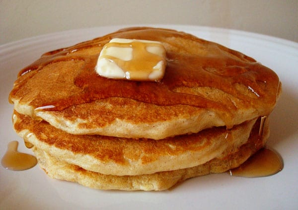 Pancakes in a stack with syrup and a pat of butter on top.