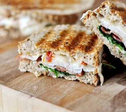 A smoked turkey club panini cut in half with one half laying slanted on the other.