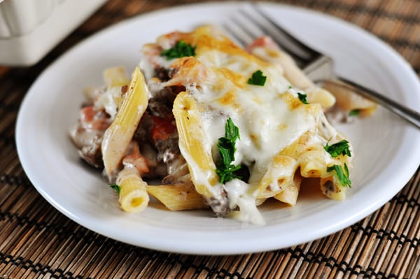 White plate with baked greek pastitio pasta, topped with melted cheese.