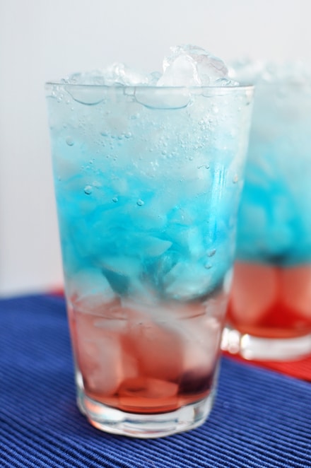 A red, white, and blue layered drink full of ice in a glass cup.