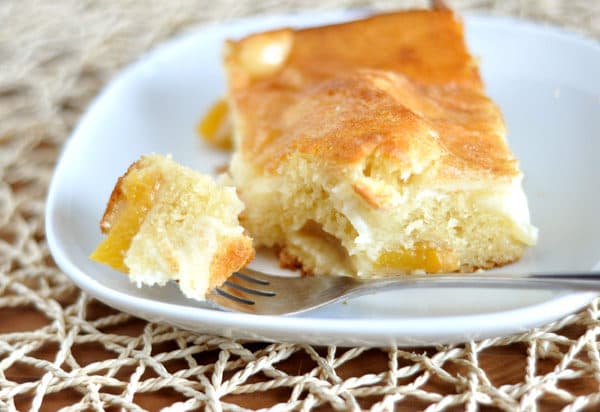 A slice of peach cake with a bite taken out on a white plate.