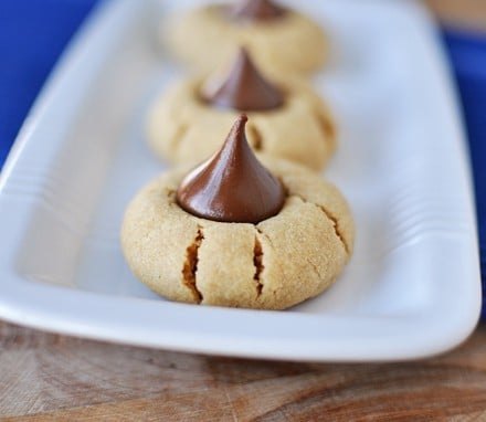 White plate with Hershey's kiss topped peanut butter cookies lined up in a row.