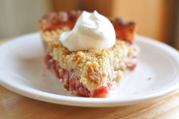 A streusel-topped, berry-filled slice of pie, with a dollop of whipped cream on the top, on a white plate.
